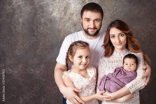 Happy family portrait. Smiling parents with two children. Mother and father with newborn baby and toddler girl. Concept of happy family. Copy space