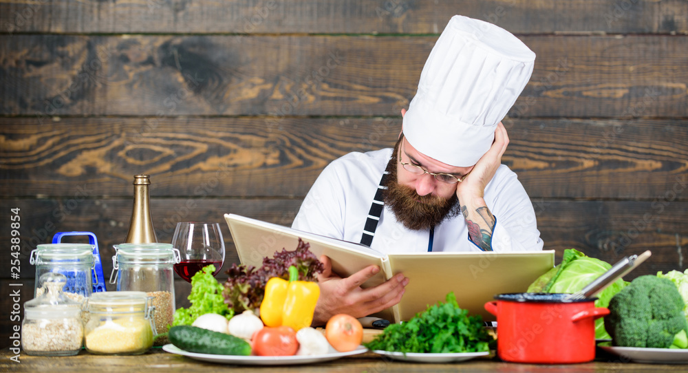 Man bearded hipster read book recipe near table fresh vegetables. Culinary arts. Recipe to cook healthy food. Experienced chef cooking excellent dish. This recipe is just perfect. Vegetarian recipe Man bearded hipster read book recipe near table fresh vegetables. Culinary arts. Recipe to cook healthy food. Experienced chef cooking excellent dish. This recipe is just perfect. Vegetarian recipe