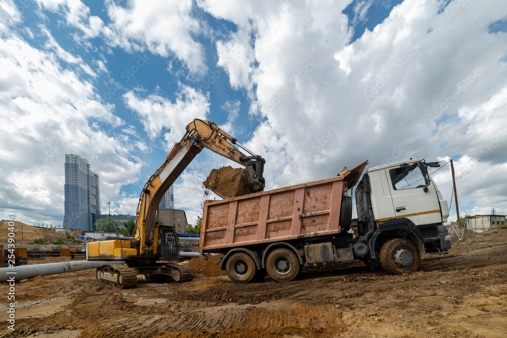 A crawler excavator overloads the sand from the embankment into a dump truck