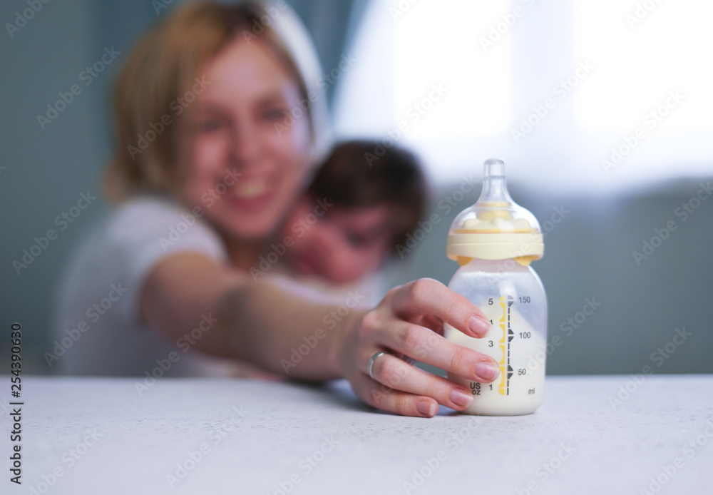 Baby bottle with breast milk for breastfeeding at foreground and mother
