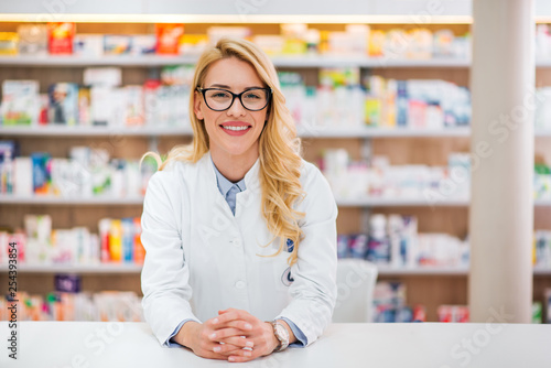 Portrait of a beautiful blonde pharmacist leaning on counter at pharmaceutical store. photo