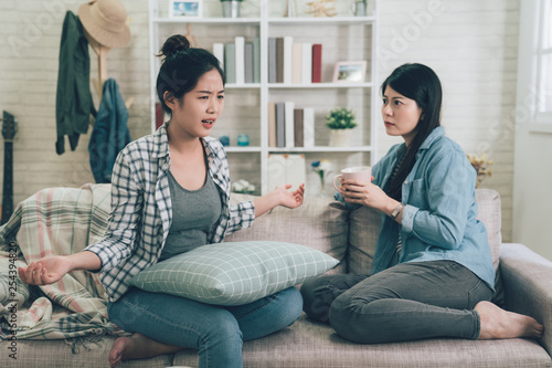 Fotografie Two female friends sitting on sofa chatting talking and drinking tea or coffee spending time together on holidays