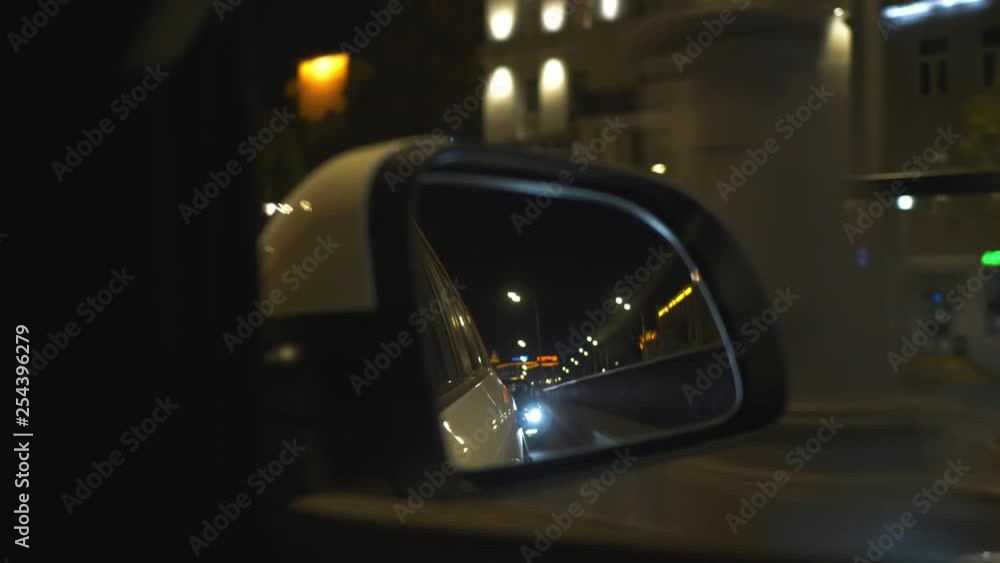 Reflection in car mirror while driving on night street. Vehicle shot with mirror reflecting traffic and lights of city driving on street in night time Reflection in car mirror while driving on night street. Vehicle shot with mirror reflecting traffic and lights of city driving on street in night time