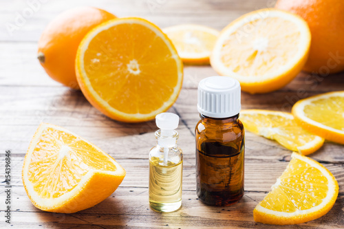 Essential orange oil in bottle, fresh fruit slices on wooden background. Natural fragrances.