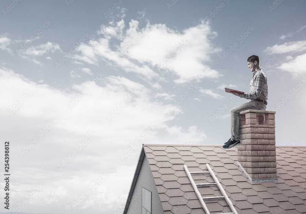 Handsome man on brick roof against cloud scape reading book Handsome man on brick roof against cloud scape reading book
