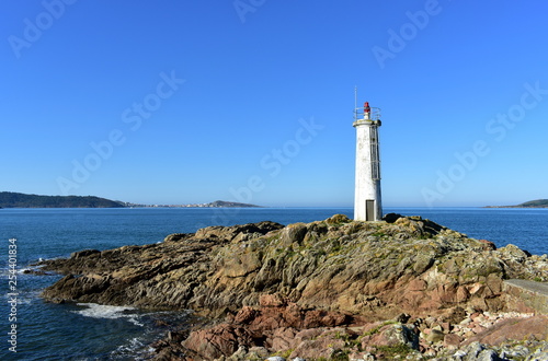 Bay with white lighthouse on the rocks. Blue sea, sunny day. Galicia, Spain.