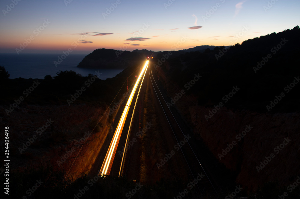 Landscape at dusk next to the Mediterranean coast with train light moving between two tunnels