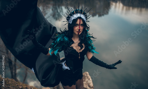 Fotografia A woman in the image of a fairy and a sorceress standing over a lake in a black dress and a crown