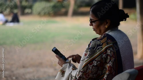 Wallpaper Mural Side angle shot of an old Indian woman sitting in a park wearing a saree looking at her smart phone Torontodigital.ca
