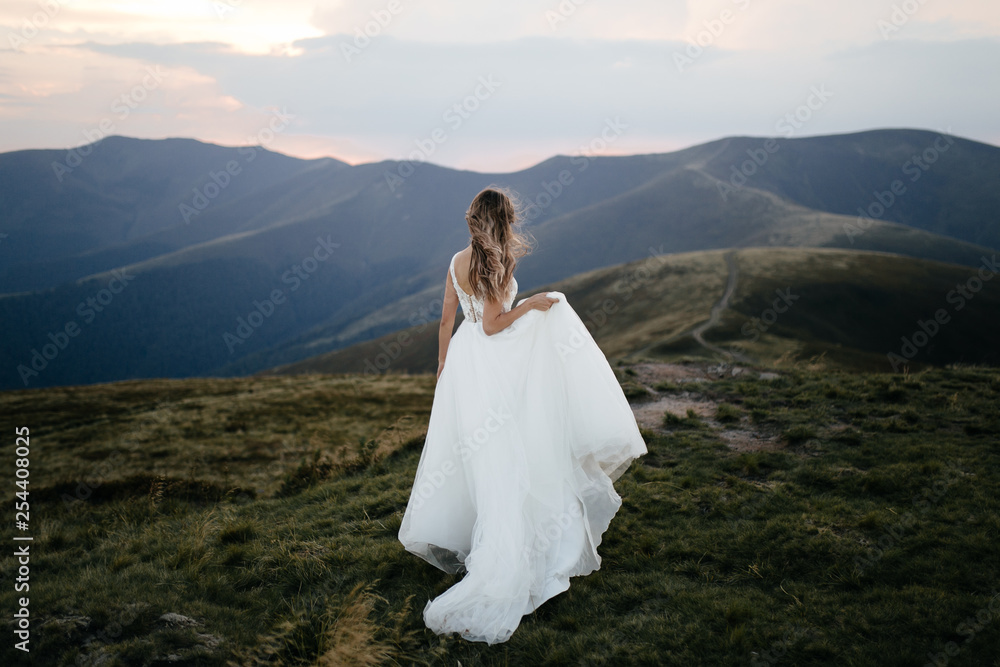 Stylish bride standing on beautiful landscape of mountains on sunset Stylish bride standing on beautiful landscape of mountains on sunset