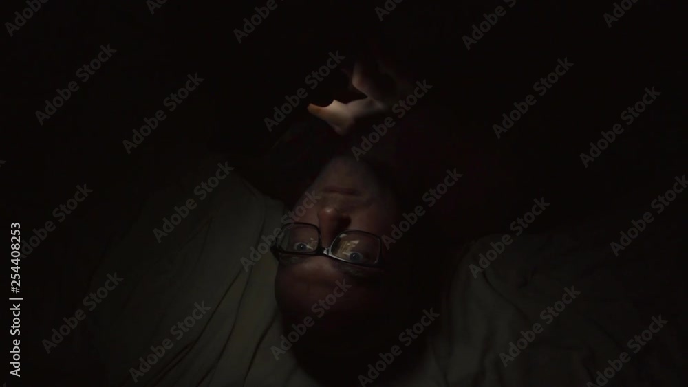 Close-up shot of a guy laying in bed at night and surfing web on smartphone. Close-up shot of a guy laying in bed at night and surfing web on smartphone.