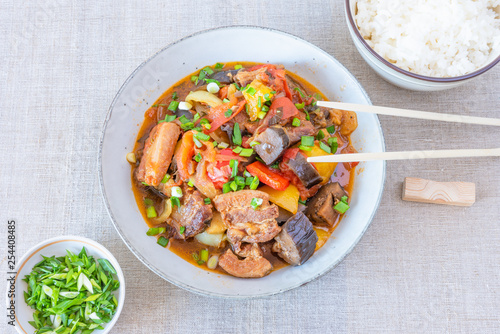 Fried pork with eggplants and sweet peppers in a large bowl and a cup of rice - a traditional Asian dish