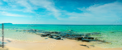 Golden sand beach by the sea with emerald green sea water and blue sky and white clouds. Summer vacation on tropical paradise beach concept. Ripple of water splash on sandy beach. Summer vibes.