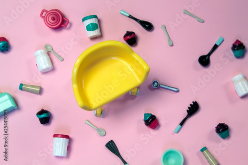 flat lay image of plastic toy tableware with cakes and empty yellow chair on pastel pink background