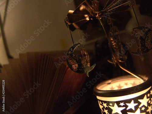 Close up view of a fairy sitting on a moon metal candle rotation carousel with stars shapes lit, in front of an open book , indoors at night. photo