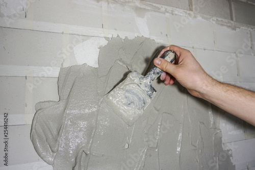 Closeup builder's hand smears cement glue on the wall with trowel to glue ceramic tiles in the bathroom. Concept renovation repair, overhaul, contract tiler