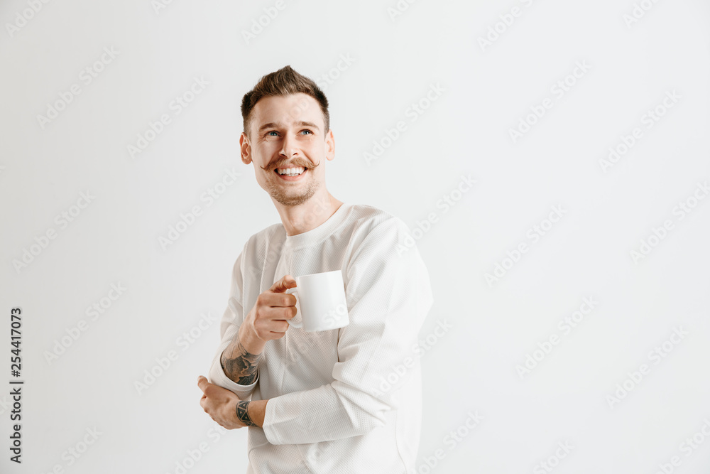 Taking a coffee break. Handsome young man holding coffee cup while standing against gray studio background Taking a coffee break. Handsome young man holding coffee cup while standing against gray studio background