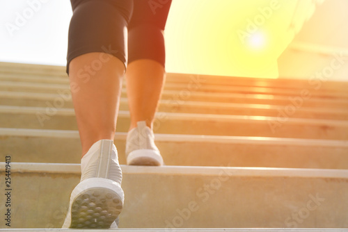 Young sport woman running up on stone stairs with sun spot background. Healthy lifestyle, workout and diet concept.