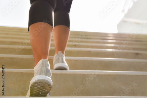 Young sport woman running up on stone stairs with sun spot background. Healthy lifestyle, workout and diet concept.