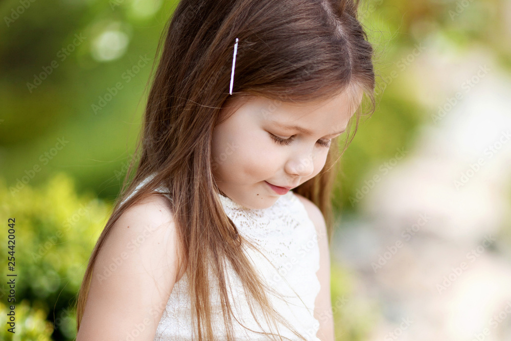 Beautiful smiling little girl in cream dress, against green of summer park Beautiful smiling little girl in cream dress, against green of summer park