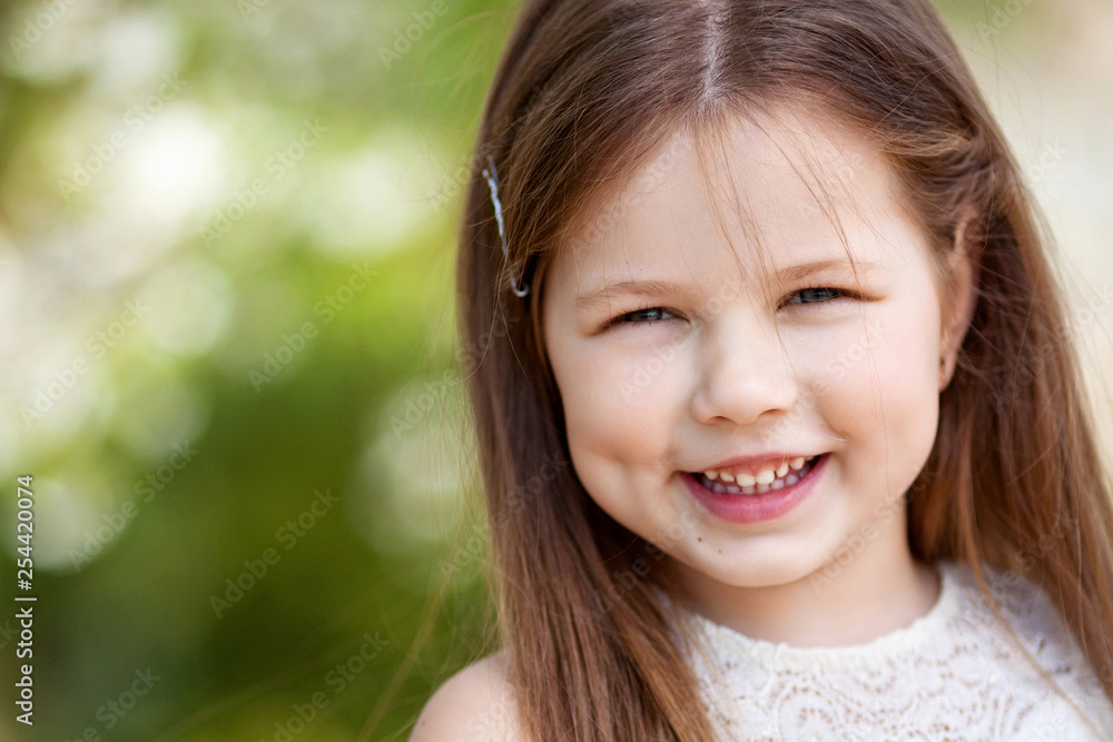 Beautiful smiling little girl in cream dress, against green of summer park Beautiful smiling little girl in cream dress, against green of summer park