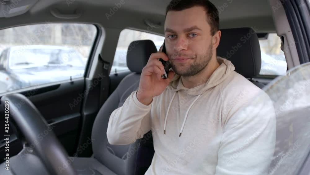 Casual handsome guy talking on the phone sitting in a car on a driver seat.