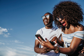 Two happy friends using the mobile in the street. Friendship concept.