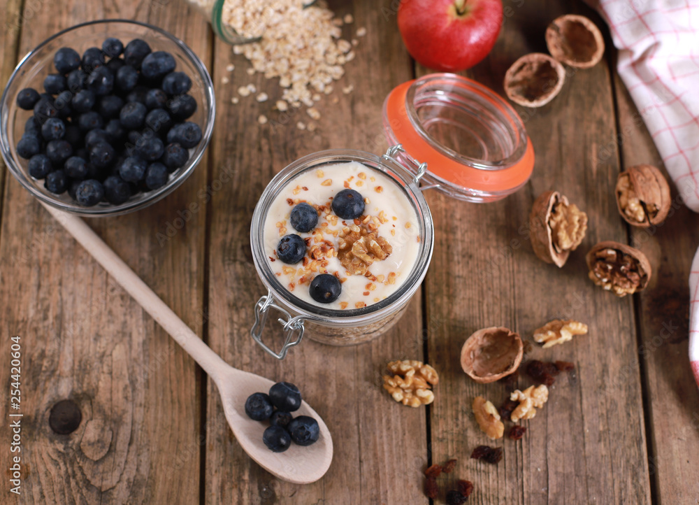 Fototapeta premium Healthy breakfast with yogurt on oatmeal muesli and walnuts, in a glas on a rustic wooden table.