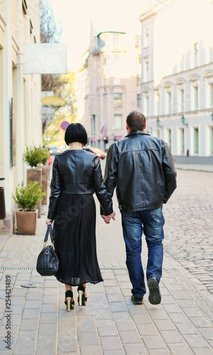 A loving couple walking the streets of old Riga, Latvia. A woman is wearing leather jacket and high heels, man is wearing leather jacket. They are holding hands.