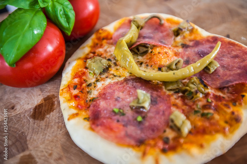 Original Italian Pizza alla diavolo on brown wood background. Pizza with Hot peppers and salami close up