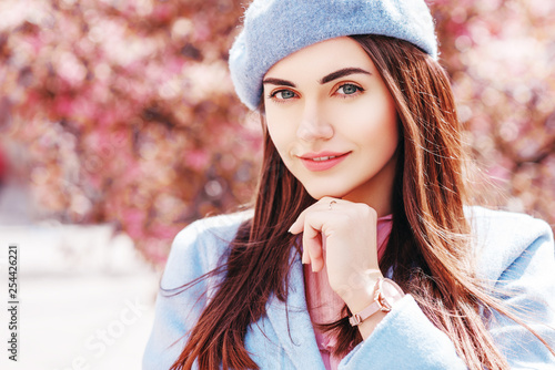 Outdoor close up portrait of  young beautiful happy smiling lady wearing stylish pastel blue color beret, coat, wrist watch, posing in spring street of European city. Copy, empty space for text