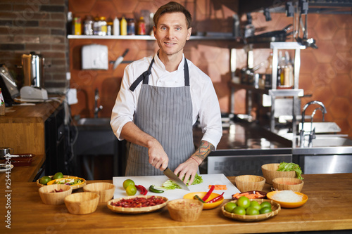 Waist up portrit of handsome chef cutting vegetables standing at table with spices  copy space