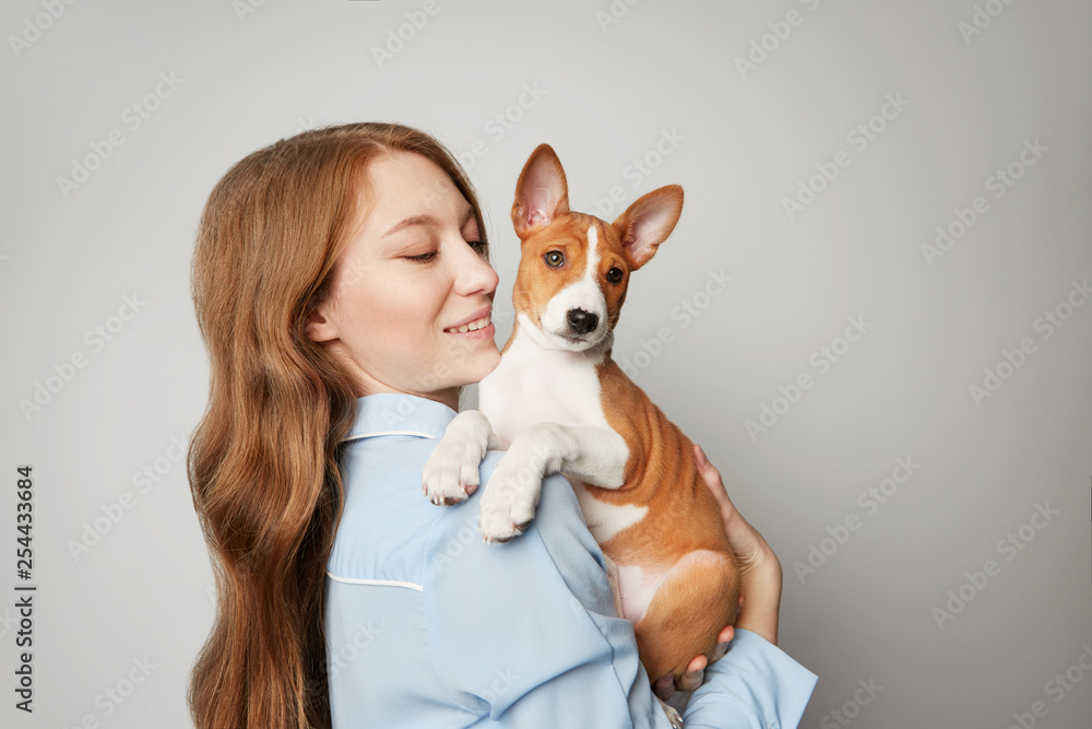 Beautiful red haired girl embracing puppy on white background. Studio portrait of white appealing woman chilling with dog. Beautiful red haired girl embracing puppy on white background. Studio portrait of white appealing woman chilling with dog.