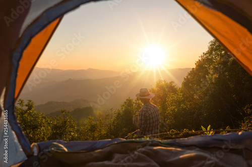 Happy man with holding coffee cup stay near tent around mountains under sunset light sky enjoying the leisure and freedom.