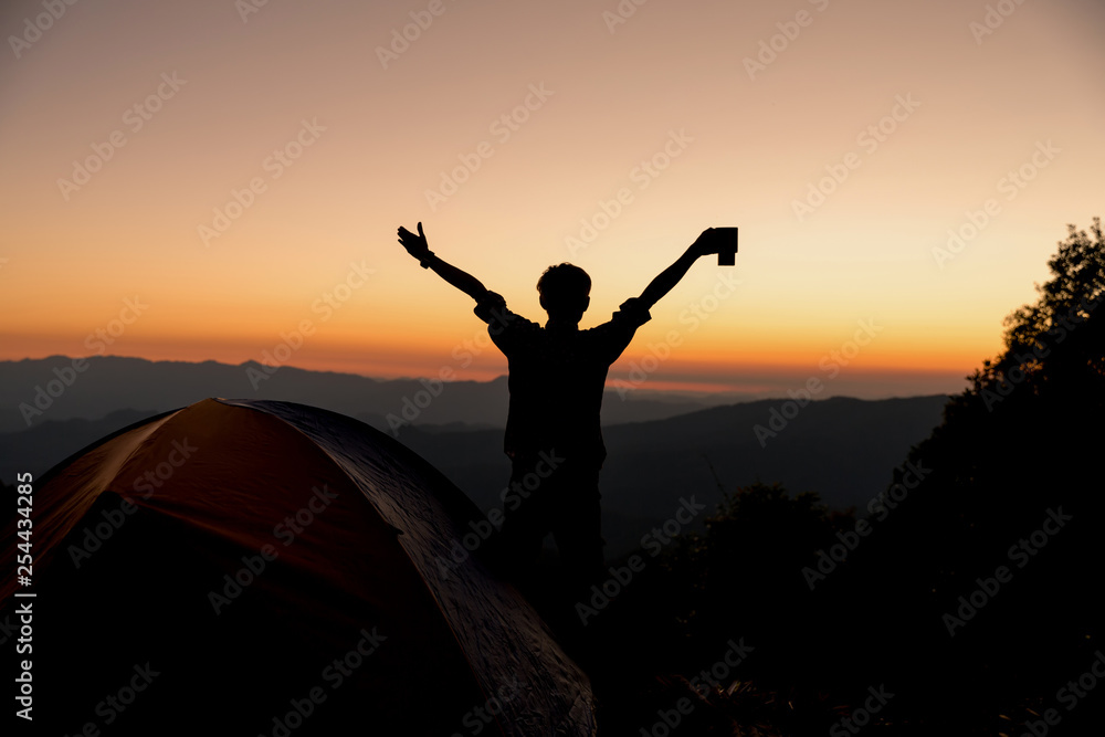 Silhouette of Happy man with holding coffee cup stay near tent around mountains under sunset light sky enjoying the leisure and freedom. Silhouette of Happy man with holding coffee cup stay near tent around mountains under sunset light sky enjoying the leisure and freedom.