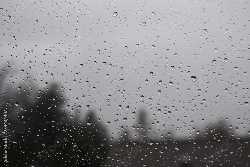 Water drops on window with blurred trees and house in background.