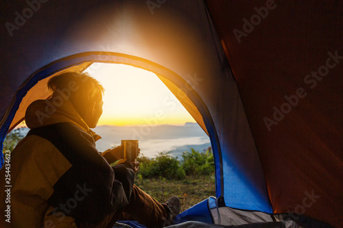 A young man sitting in the tent with holding coffee cup, looking at the mountain landscape in winter.Light effects