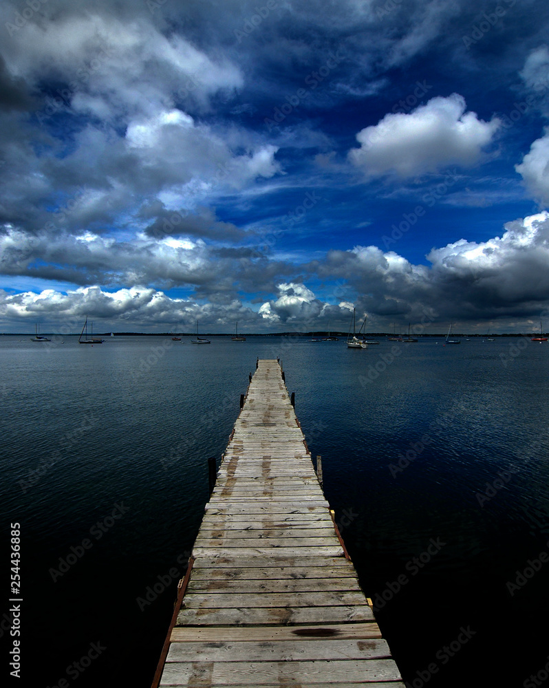 Fototapeta premium Old Wooden Dock out in Water with Sky Clouds Lake