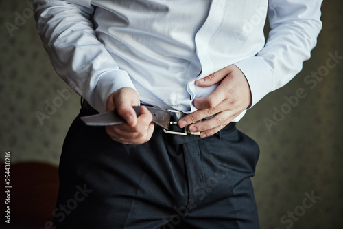 Businessman putting on a belt, fashion and clothing concept,groom getting ready in the morning before ceremony