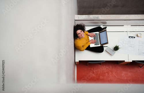 A top view of young businesswoman sitting on desk in an office, using laptop. photo