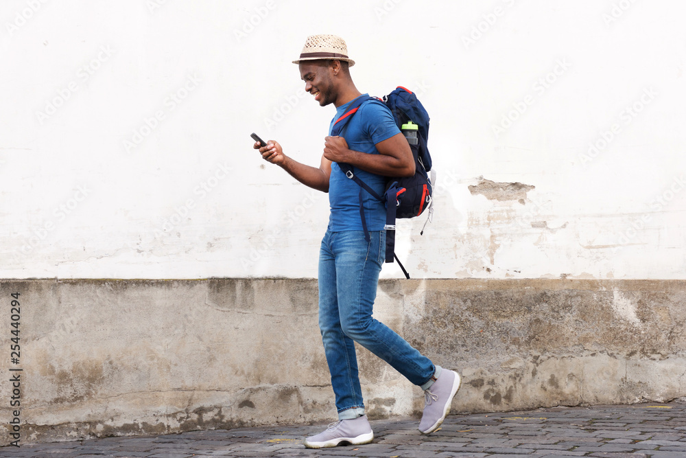 Φωτογραφία side portrait of happy african american tourist man walking with bag and cellpho