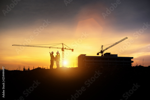 Silhouette engineer construction work control and tower crane background on natural sunset sky.,Heavy industry and building construction work concept