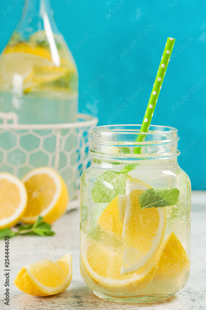 Fototapeta premium Fresh lemonade in mason jar. Mint and lemon halves on blue fresh background