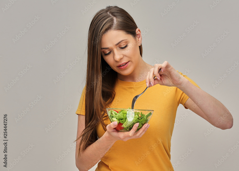 girl wearing yellow T-shirt eating salad with lettuche from glass bowl. isolated studio portrait. girl wearing yellow T-shirt eating salad with lettuche from glass bowl. isolated studio portrait.
