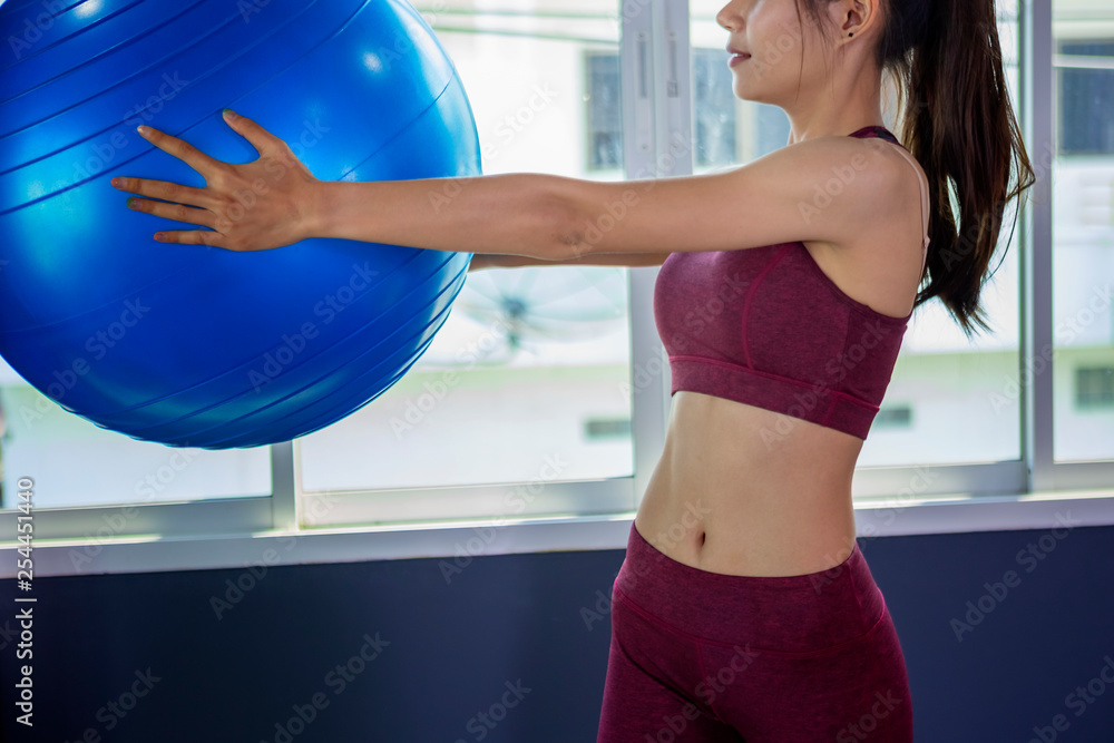 Beautiful woman is exercising by playing Pilates ball happily in a public gym.