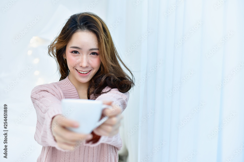 Winter Concept. Beautiful woman is relaxing in a white bedroom. Beautiful woman in a winter dress is eating coffee in the bedroom. Winter Concept. Beautiful woman is relaxing in a white bedroom. Beautiful woman in a winter dress is eating coffee in the bedroom.