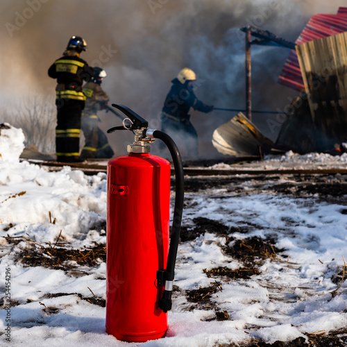 Mechanical foam fire extinguisher closeup on the background of fire and firemen. A team of firefighters at work on the fire.