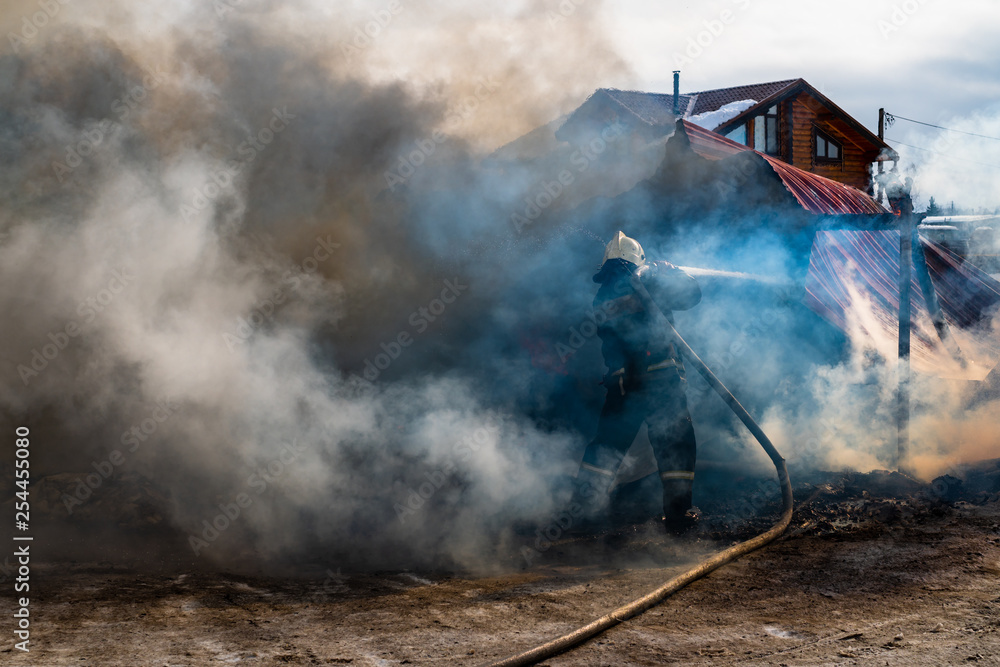 Fototapeta premium Firemen extinguishes a burning old wooden residential house. Firefighters at work on the fire. Fireman with a hose puts out the fire with water