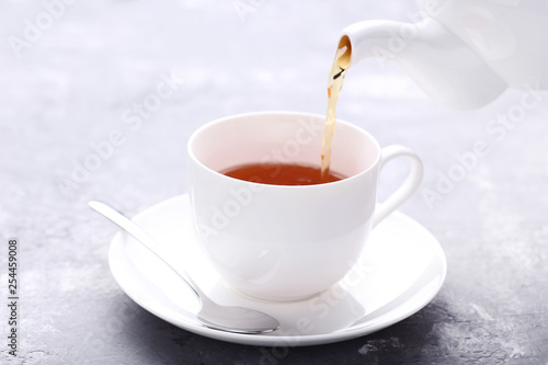 Pouring tea from teapot in white cup on wooden table