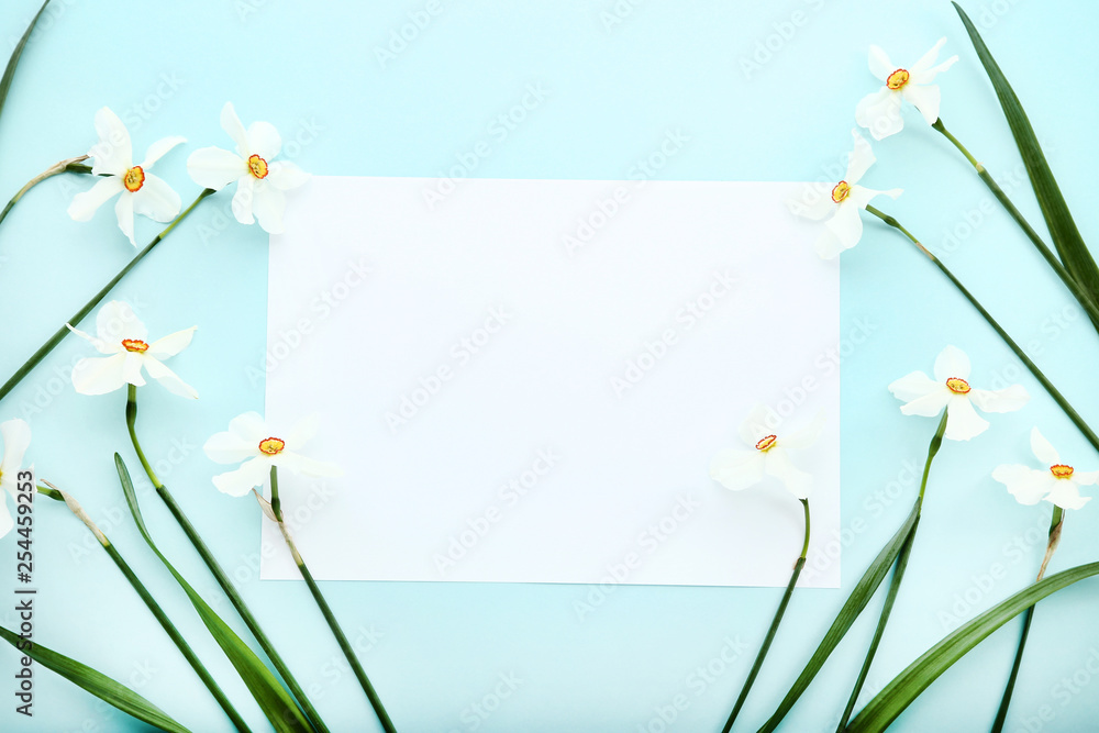 Obraz premium White narcissus flowers with blank sheet of paper on blue background